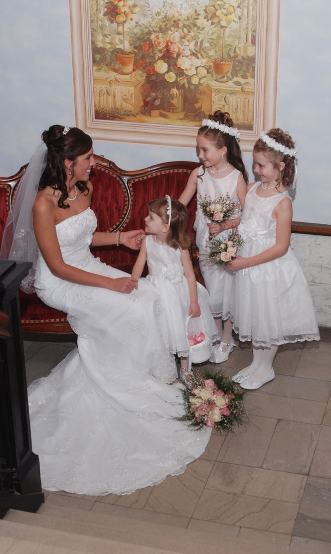 Bride with three small children on red sofa in marble entrance at The Corinthian Event Center.
