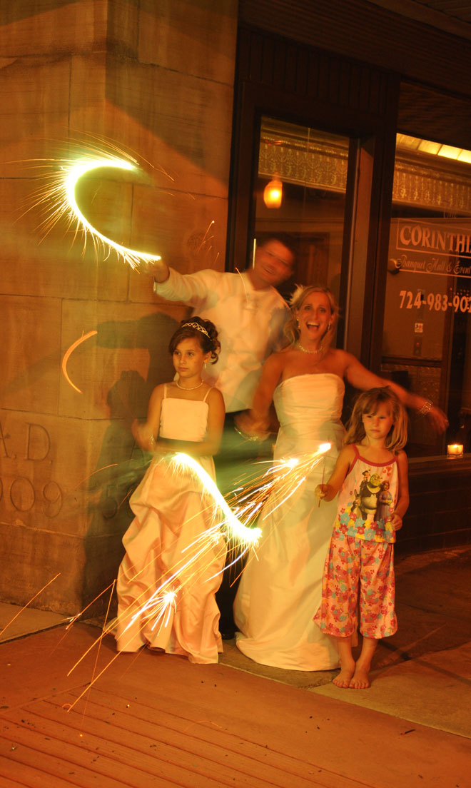 Bride and Groom and children with sparklers at night in the main entrance to The Corinthian Event Center.