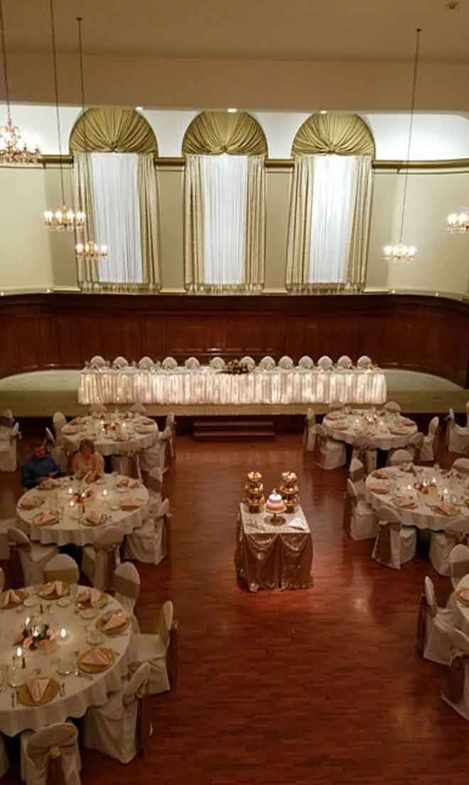 Grand Ballroom setup in gold and white theme with chair covers, candle in flower ring decor centerpieces, and gold plate place settings at The Corinthian Event Center.