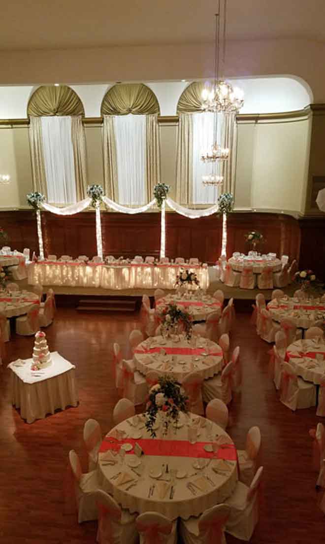 Grand Ballroom setup in pink and white theme with chair covers, flower decor centerpieces, and white plate place settings at The Corinthian Event Center.