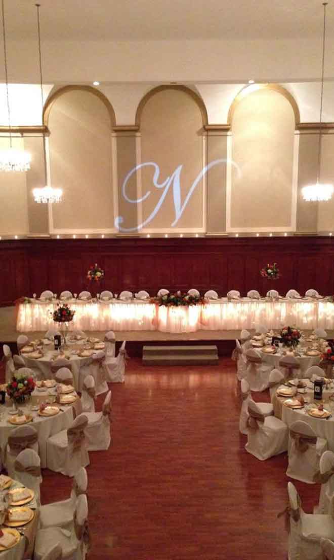 Grand Ballroom setup in gold and white theme with chair covers, flower decor centerpieces, and gold plate place settings at The Corinthian Event Center.