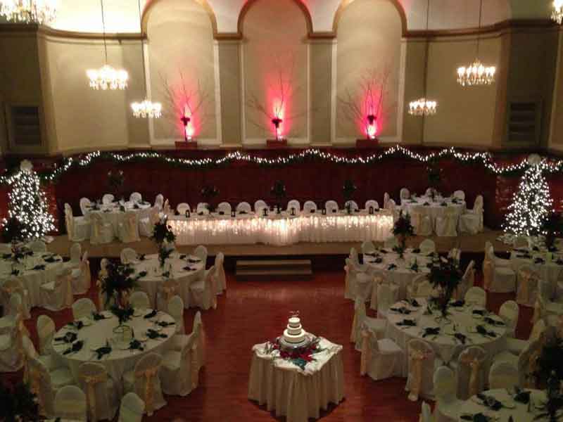 Grand Ballroom setup in white and peach Christmass theme with chair covers, flower centerpieces, and white plate place settings at The Corinthian Event Center.