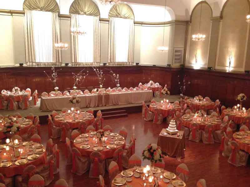 Grand Ballroom setup in pink and white theme with chair covers, flower and candle centerpieces, and gold plate place settings at The Corinthian Event Center.