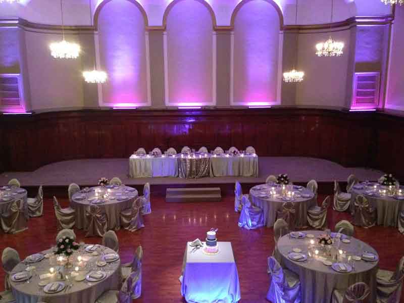 Grand Ballroom setup in grey and pink theme with chair covers, flower and candle centerpieces, and white plate place settings at The Corinthian Event Center.
