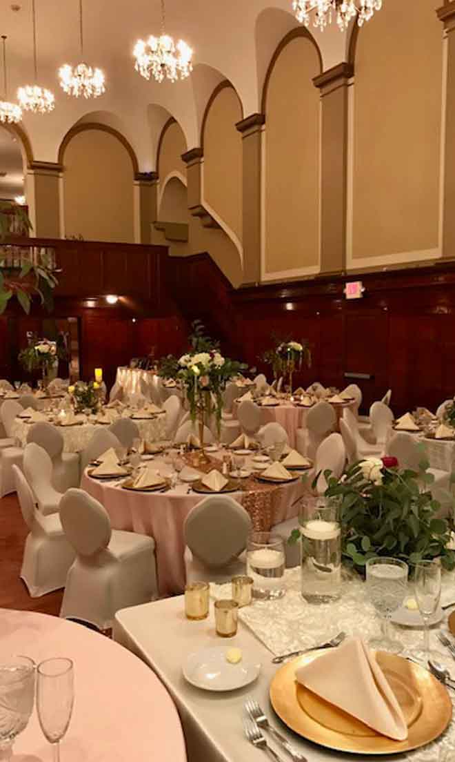 Grand Ballroom setup in pink and white theme with chair covers, flower decor centerpieces, and gold plate place settings at The Corinthian Event Center.