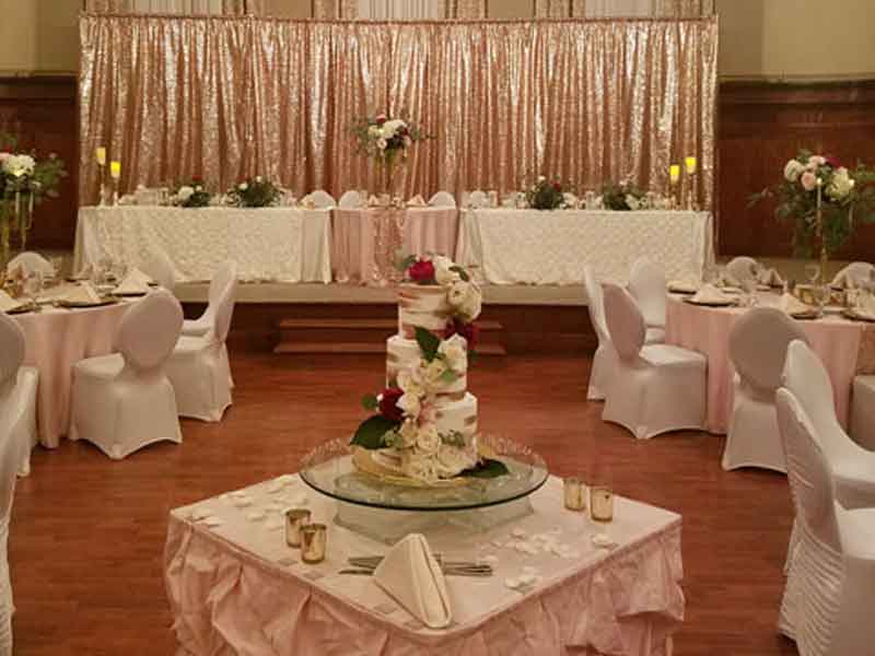 Grand Ballroom setup in white and pink theme with chair covers, flower centerpieces, a backdrop at the head table, and grey plate place settings at The Corinthian Event Center.