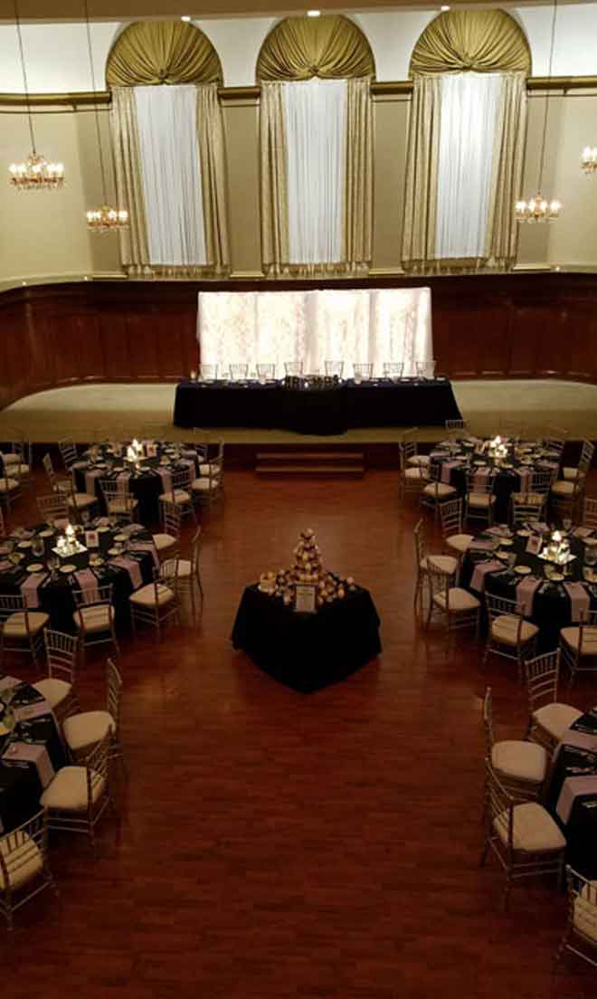 Grand Ballroom setup with stage backdrop in black and purple theme with candle decor centerpieces and white plate place settings at The Corinthian Event Center.