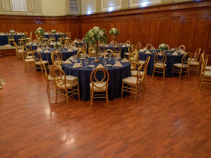 Grand Ballroom setup in blue and gold theme with flower centerpieces, and white place settings at The Corinthian Event Center.